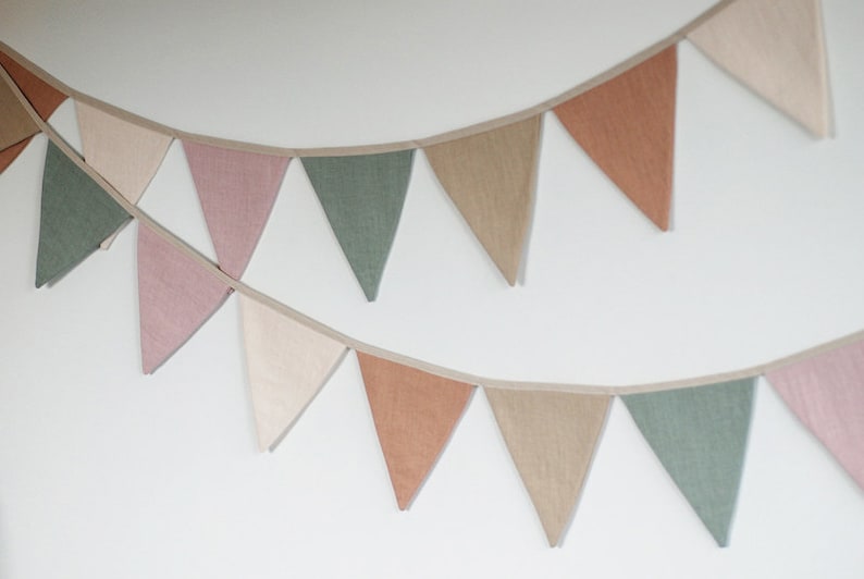 Puede incluir: Una guirnalda de banderines de tela con banderas triangulares en tonos rosa, verde, beige y marr&oacute;n. Las banderas est&aacute;n cosidas juntas con una cuerda blanca.
