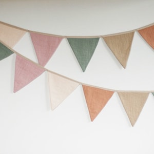 Puede incluir: Una guirnalda con banderas triangulares en tonos rosa, verde y marr&oacute;n. Las banderas est&aacute;n hechas de una tela texturizada y est&aacute;n enhebradas con una cinta blanca.