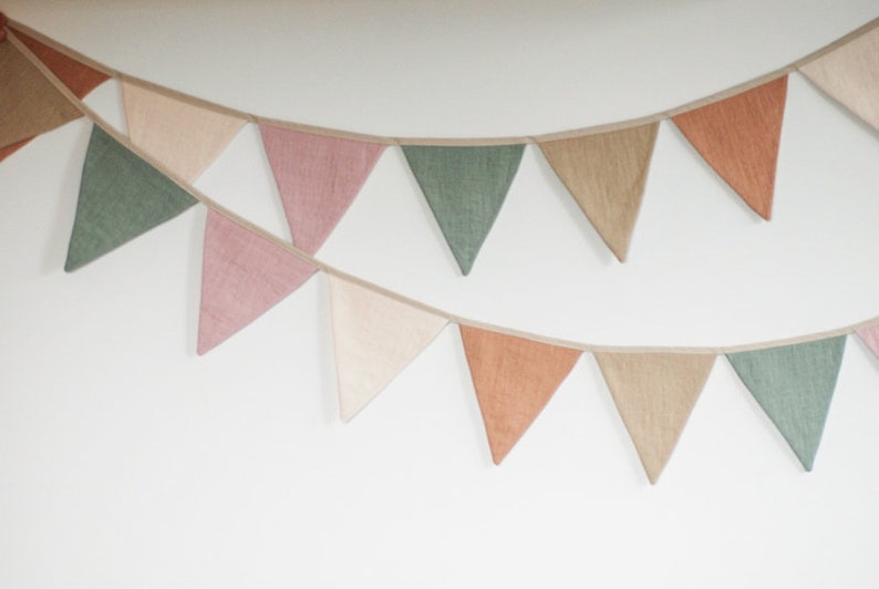 Puede incluir: Una guirnalda con banderas triangulares en tonos rosa, verde y marr&oacute;n. Las banderas est&aacute;n hechas de una tela texturizada y est&aacute;n enhebradas con una cinta blanca.