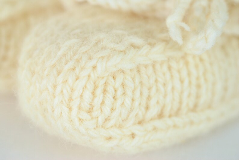 May include: Close-up of a knitted cream-colored fabric with a textured pattern. The fabric is soft and fluffy, with a subtle sheen.