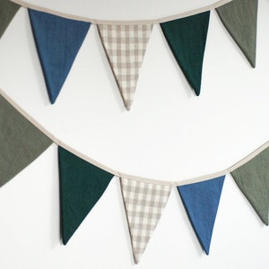 May include: A bunting with alternating green, blue, and beige triangle flags. The flags are made of fabric and have a white trim.