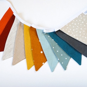 Peut inclure: Une bannière en tissu colorée avec dix drapeaux triangulaires. Les drapeaux sont dans des tons d'orange, rouge, beige, jaune, marron, bleu et gris. Certains drapeaux ont des pois blancs.