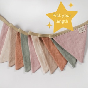 Könnte beinhalten: Eine Girlande mit acht dreieckigen Flaggen in verschiedenen Schattierungen von Rosa, Beige und Grün. Die Flaggen sind aus einem weichen, strukturierten Stoff gefertigt und mit einem beigefarbenen Band verbunden. Der Text "Pick your length" ist auf einem gelben Stern geschrieben.