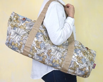 May include: A large, beige and brown tote bag with a butterfly and floral print. The bag has two long, brown straps and a light blue lining.