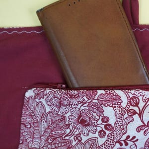 May include: A burgundy tote bag with a brown leather wallet partially visible. A patterned zippered pouch with a floral design in white and burgundy is in the front pocket. Keys and a coin are also visible.