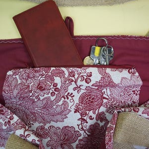 May include: Burgundy tote bag with a floral patterned pocket. A matching burgundy wallet and a set of keys are visible inside the bag. The bag has wooden button closures and a neutral-colored burlap trim.