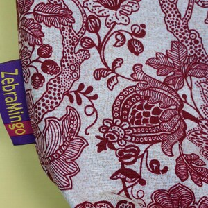 May include: Close-up of fabric with a floral pattern in burgundy and off-white. The design features stylized flowers, leaves, and branches. A purple tag with the text "ZebraMingo" is attached to the fabric.
