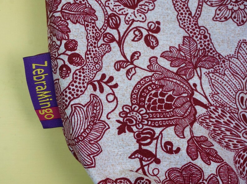 May include: Close-up of fabric with a floral pattern in burgundy and off-white. The design features stylized flowers, leaves, and branches. A purple tag with the text "ZebraMingo" is attached to the fabric.