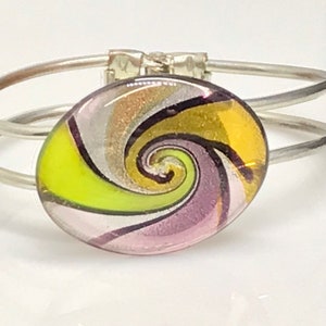May include: A silver bangle bracelet featuring a colourful glass swirl design. The glass is yellow, green, pink and white with black lines.