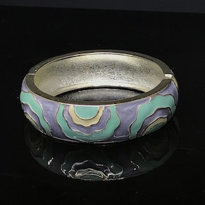 May include: A silver bangle bracelet with a colorful abstract design. The design features swirls of purple, green, and cream.
