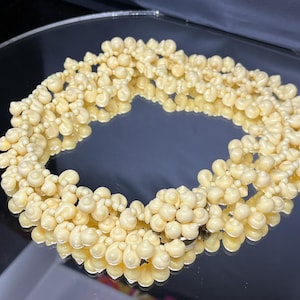May include: A multi-strand necklace made of cream-colored plastic beads. The beads are shaped like small, rounded shells.