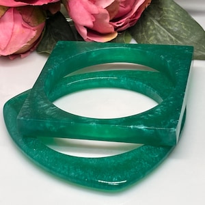 Op de afbeelding: Twee groene hars armbanden, een vierkant en een gebogen, met een marmer effect.