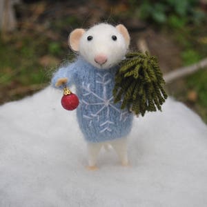 May include: A white felt mouse wearing a blue sweater with a snowflake design, holding a red ornament and a green felt sprig.