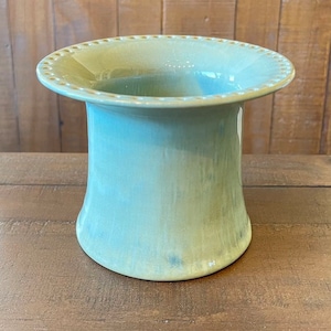May include: A light green ceramic vase with a wide, flared rim and a cylindrical body. The rim is decorated with small, evenly spaced dots. The vase has a smooth, glossy finish and a gradient of colors, transitioning from a lighter green at the top to a darker green at the base.