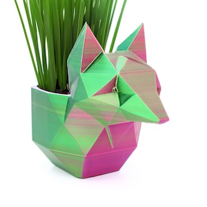 May include: A geometric fox-shaped planter made of green and pink plastic. The planter is filled with green grass.