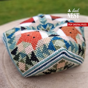 May include: A square, hand-stitched textile with a fox design. The fox is orange with black details, set against a backdrop of blue, green, and white geometric patterns. The edges are finished with a striped border. The text "PDF DIGITAL FILES" is visible.