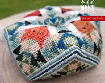 May include: A multi-sided, stuffed fabric object featuring a cross-stitch pattern of orange foxes, green foliage, and blue accents. The design includes the text little NEST emporium and PDF DIGITAL FILES. The object has a geometric, dimensional shape.