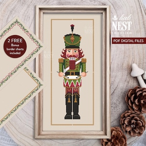 Könnte beinhalten: Ein gerahmtes Kreuzstichmuster eines Nussknacker-Soldaten in Grün, Rot und Gold. Das Bild enthält den Text "Little Nest Emporium" und "PDF DIGITAL FILES". Zwei zusätzliche Bordüren sind enthalten.