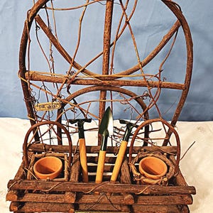 May include: A rustic, wooden garden display with a large wheel-like structure and a lower section with small terracotta pots and gardening tools. The sign reads "Bloom where you are planted."