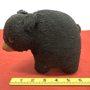 May include: A vintage black bear plush toy with a brown snout and small, round eyes. The bear is standing on all fours and has a slightly worn appearance. The toy is approximately 6 inches long.