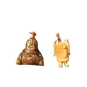 May include: Two pendants are displayed against a white background. One is a seated Buddha figure in shades of green and brown. The other is a gold-colored pendant of a standing figure with arms raised.
