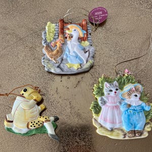 Peut inclure: Trois décorations de Noël en porcelaine représentant un canard avec deux poussins, deux chats et une tortue. Les décorations sont peintes dans des couleurs vives et ont un style vintage.