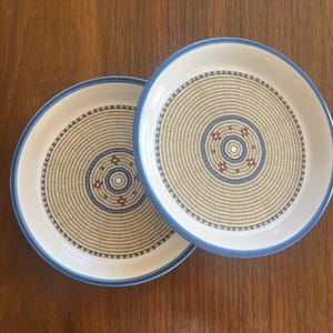 May include: A white ceramic mug with a black handle and the text "But First, Coffee" in a bold, black font. The mug is set against a blurred background, suggesting a cozy setting.