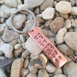 May include: A copper keyring with a silver key ring. The keyring has the coordinates 52.21.57.3&deg; N 1.20.11.3&deg; W engraved on it.