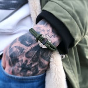 May include: A green paracord bracelet with a silver circular charm featuring the numbers 61, 30, 4, 9, 1, 1, 6.
