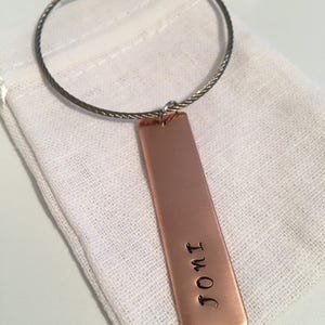 May include: A copper keychain with a silver cable chain and a rectangular tag engraved with the text "I OMT".