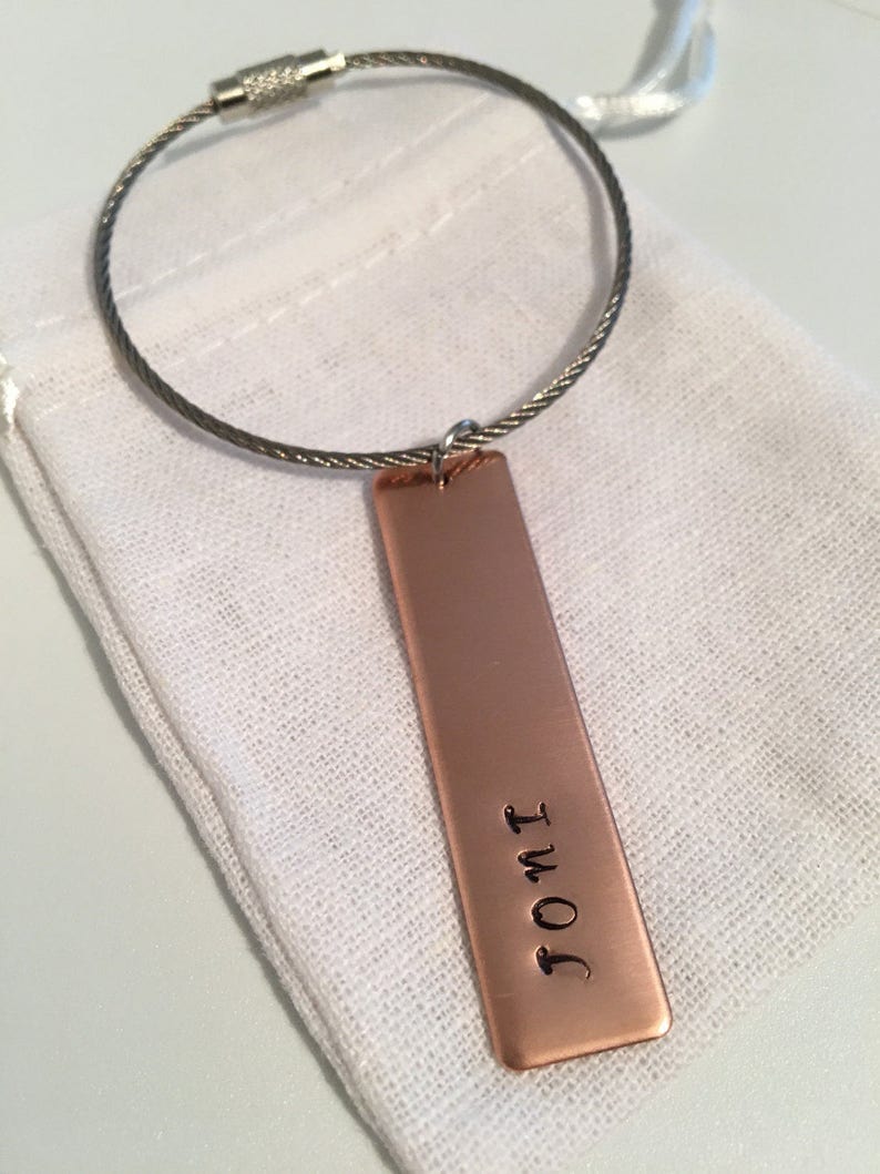 May include: A copper keychain with a silver cable chain and a rectangular tag engraved with the text "I OMT".