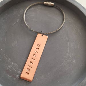 May include: A copper keychain with a silver cable chain and a rectangular tag engraved with the date "29/11/2010".