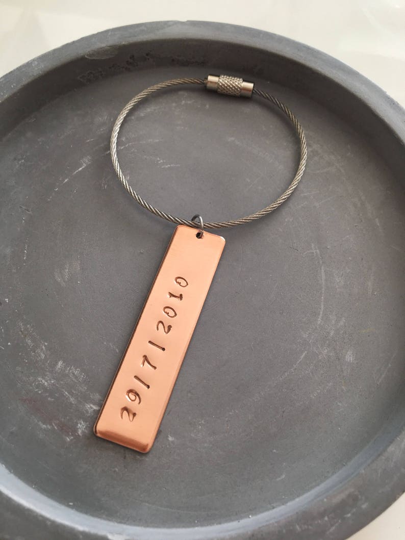 May include: A copper keychain with a silver cable chain and a rectangular tag engraved with the date "29/11/2010".
