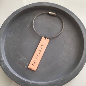 May include: A copper keychain with a silver cable chain and a rectangular tag engraved with the date "2017112010".