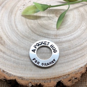 May include: A silver metal charm with the text "A Pocket Hug For Granny" engraved on it.