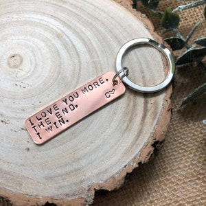 May include: A copper-coloured keychain with a silver ring. The keychain has the text "I love you more. The end. I win." engraved on it. There is a small heart symbol at the end of the text.