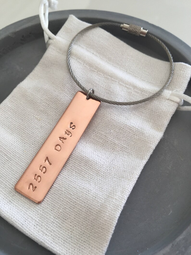 May include: A copper keychain with a rectangular tag engraved with the text "2557 Days" hanging from a silver cable chain.