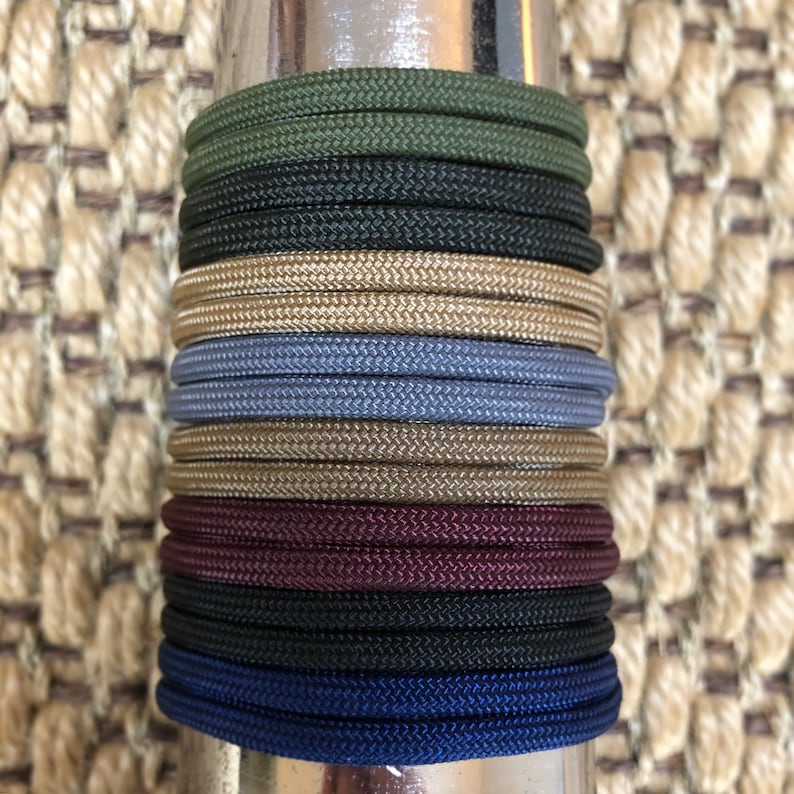 May include: A stack of different colored paracord bracelets. The bracelets are made of a variety of colors, including green, black, gold, blue, brown, burgundy, and navy blue.