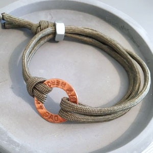 May include: Olive green paracord bracelet with a copper ring charm that reads "MY HERO".