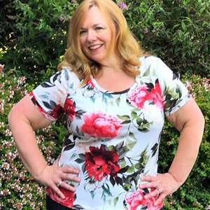 May include: A woman wearing a white floral print short-sleeved shirt with red, pink, and green flowers and black leggings.