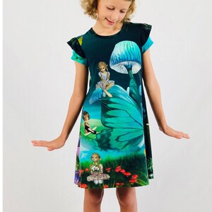 Könnte beinhalten: Dunkel türkisfarbenes Kleid mit einem märchenhaften Design. Das Kleid zeigt einen großen Schmetterlingsflügel, Pilze und Feen. Das Kleid hat kurze Ärmel und wird mit einem Perlenstirnband und schwarzen Schuhen getragen.