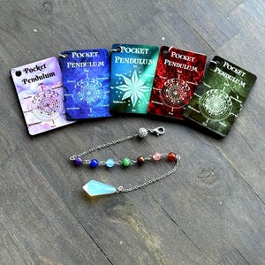 Puede incluir: Cinco tarjetas rectangulares Pocket Pendulum en morado, azul, turquesa, rojo y verde, cada una con un gráfico circular. Una cadena de metal plateado con siete pequeñas cuentas multicolores y una punta de cristal facetado translúcido.
