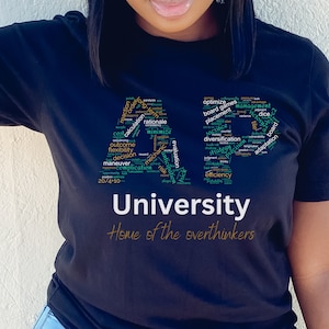 May include: Black t-shirt with a word cloud design in the shape of the letter "A" and the text "University Home of the overthinkers". The word cloud includes words like "optimize", "placement", "diversification", "strategy", and "efficiency".