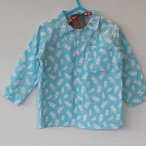 Op de afbeelding: Lichtblauw pyjamashirt met een patroon van witte ijsberen. Het shirt met lange mouwen heeft een kraag, een borstzak en een knoopsluiting. Het label luidt "Dotty".
