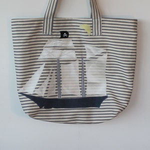 May include: A striped tote bag with a white sailboat applique and a skull and crossbones design. The bag has blue and white stripes.