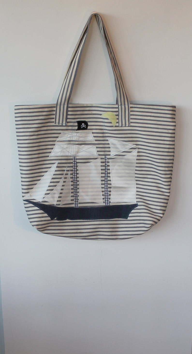 May include: A striped tote bag with a white sailboat applique and a skull and crossbones design. The bag has blue and white stripes.