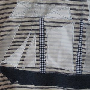 May include: A white and blue striped fabric with a white applique of a sailboat. The sailboat has a black and white checkered mast and a blue denim hull.