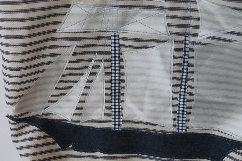 May include: A white and blue striped fabric with a white applique of a sailboat. The sailboat has a black and white checkered mast and a blue denim hull.