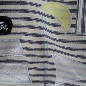 May include: A white and blue striped fabric with a black patch featuring a white skull and crossbones. The fabric has several white patches sewn on top of it.