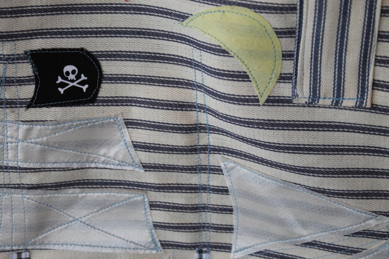 May include: A white and blue striped fabric with a black patch featuring a white skull and crossbones. The fabric has several white patches sewn on top of it.
